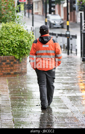 Post Officer worker returning home afte a night shift walking in the rain along a wet street in the town of Mold, Flintshire,Wales, UK Stock Photo