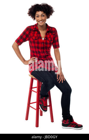 Studio shot of a relaxed young woman sitting on red stool. Stock Photo