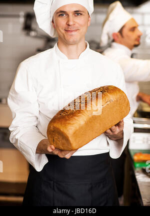Smiling male chef showcasing freshly baked whole grain bread with sesame toppings Stock Photo