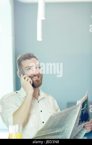 Handsome businessman with newspaper talking on cellphone Stock Photo