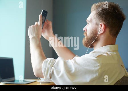 Young man with earphones talking through video-chat by smartphone Stock Photo