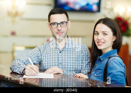 Young couple filling in registration form on arriving to hotel Stock Photo