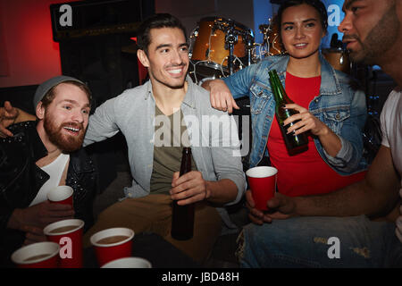 Group of smiling young people enjoying party in small night club drinking beer and chatting Stock Photo