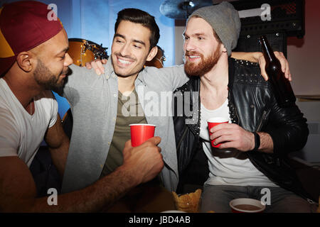 Three smiling young  men enjoying party in club, drinking beer and chatting Stock Photo