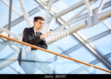 Young agent with smartphone messaging while leaning against railing Stock Photo