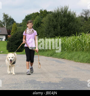 Ein Mädchen geht mit einem Golden Retriever Hund an der Leine Gassi Stock Photo