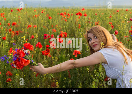 Beautiful funny woman in poppy field holding a bouquet of poppies Stock Photo