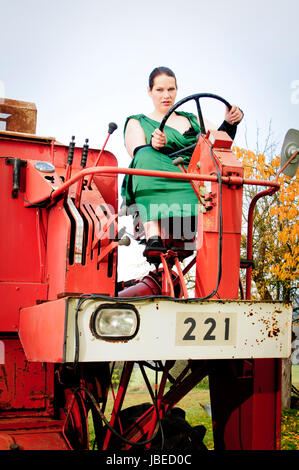 Erwachsene Frau im eleganten Abendkleid arbeitet in der Landwirtschaft und fährt einen großen Mähdrescher. Stock Photo