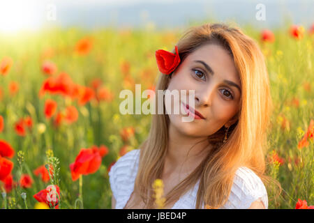Portrait of blonde woman in white dress standing on field of poppies Stock Photo