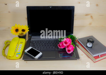 Working desk with many flowers on the laptop, phone, clock Stock Photo