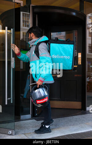 Deliveroo takeaway food delivery Courier motor cyclist collecting a delivery from a restaurant in Royal Leamington Spa. U.K. (88) Stock Photo