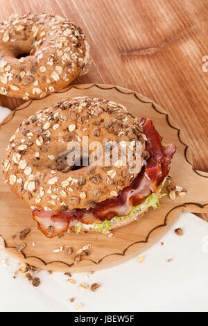 Delicious bagel eating. Whole grain bagel with bacon on wooden background. Stock Photo