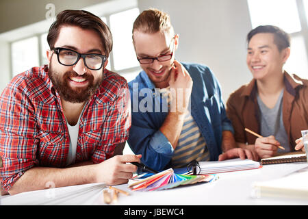 Friendly guys choosing colors from palette, bearded man in eyeglasses looking at camera Stock Photo