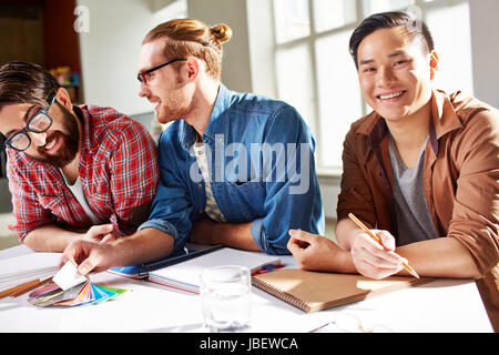 Friendly guys choosing colors from palette, Asian man looking at camera with smile Stock Photo