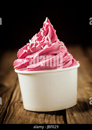 Twirl of delicious berry ice cream or frozen yoghurt in a plastic takeaway tub sprinkled with desiccated coconut against a dark background , close up side view Stock Photo