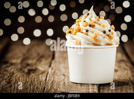 Delicious frozen yogurt party dessert twirled in a tub and decorated with sprinkles against a sparkling bokeh of festive lights Stock Photo