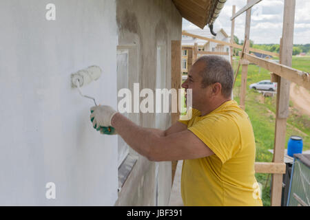The man paints the wall with a roller in white Stock Photo