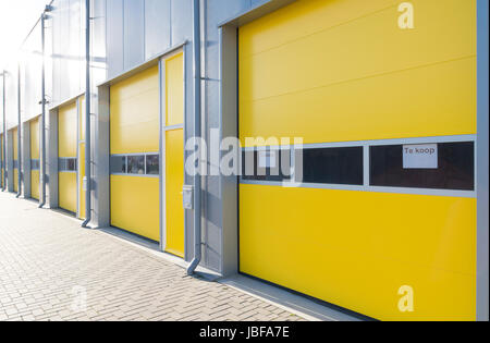 commercial warehouse with yellow roller doors with a for sale shield Stock Photo