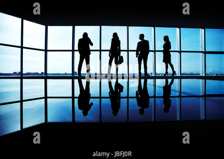 Silhouettes of several office workers standing by the window and looking at their colleague speaking on the phone Stock Photo