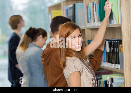 Student choosing book from bookshelf with friend in college library Stock Photo