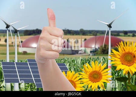 biogas facility with sunflowers and wind turbine with solar panel and hand with thumbs up Stock Photo