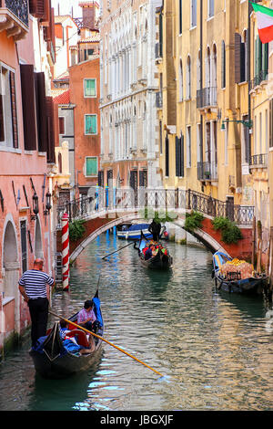 Gondolier rowing gondola with tourists on narrow canal in Venice, Italy. Venice is situated across a group of 117 small islands that are separated by  Stock Photo