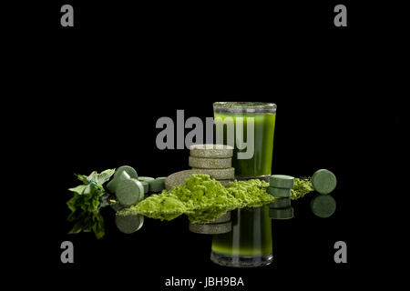 Spirulina, chlorella, wheatgrass and barleygrass blades, pills, ground powder and green juice in glass isolated on black background. Alternative medicine. Stock Photo