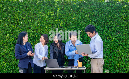 Businesswoman and businessman meeting outside office using laptop computer mobile phone and tablet device at green leaf wall,mobile office concept. Stock Photo