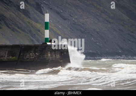 Aberystwyth Wales UK, Sunday 11 June 2017  UK Weather: Two people standing on the harbour wall as waves crash around them on a blustery summer sunday afternoon in Aberystwyth  on the Cardigan Bay coast of west  Wales  Photo credit: Keith Morris / ALAMY Live News