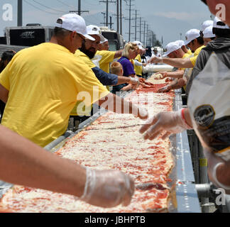 June 10, 2017. Fontana CA. The worlds longest pizza makes it into the Guinness Book of World Records as the 1.3 mile(6,820 ft) long pizza event took place at the Auto Club Speedway in Fontana California Saturday. The cooking of the pizza started at 11am and finish at 4pm outside the race track. The making of the pizza started Friday at 7pm with the pizza dough being made, cook and laid out along a 1.3 mile lone table. The making of the pizza consist of 530 gallons of tomato sauce, 20,000 pounds of dough, 15,000 pounds of cheese, 1.3 mile long table, 3 mobile pizza ovens, hundreds of pizza box Stock Photo
