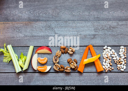 The word 'Vegan' written with vegetables, fruits, nuts and legumes on rustic wooden background, concept - organic ingredients for healthy vegan food a Stock Photo