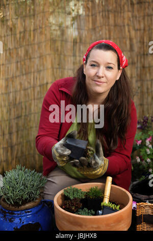 Woman gardening with different plants in front of a bamboo fence. Stock Photo