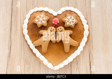 Close up of a cute Gingerbread heart decorated with Gingerbread Men, Gingerbread Stars and a Christmas Tree Cookie on light brown wooden background. Stock Photo