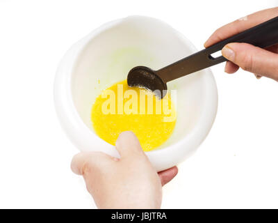 Female person mixing egg yolk and melted butter in a white bowl with a black spatula Stock Photo