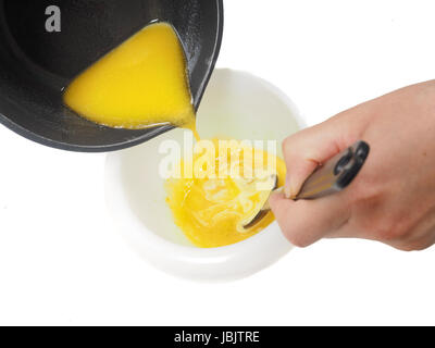 Person adding melted butter from kettle into blend in plastic bowl whilst stirring Stock Photo