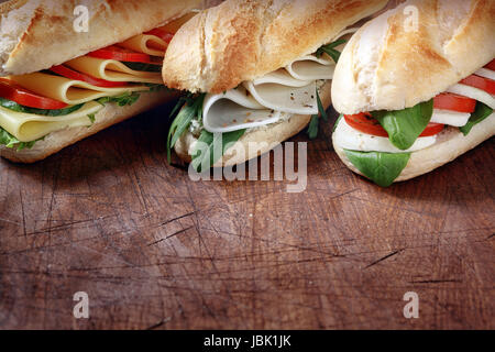 Trio of tasty vegetarian baguettes with assorted cheese fillings with basil, rocket, tomato and lettuce on crusty freshly baked rolls, rustic wooden tabletop with copyspace Stock Photo