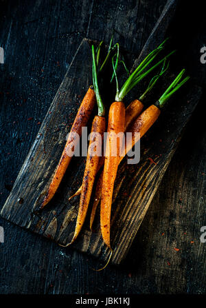 Pile of fried fresh young whole carrots ready to be eaten served on an old grungy rustic wooden board, overhead view Stock Photo