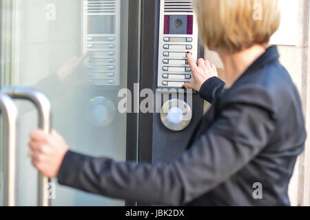 Middle aged woman pushing button of intercom Stock Photo