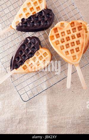 Romantic heart shaped waffle lollipops with a crisp golden wafer dipped on one side in dark chocolate cooling on a wire tray in a kitchen for Valentines or an anniversary Stock Photo