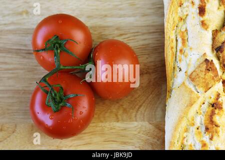 fresh tomatoes next to a crispy baguette on a wooden table Stock Photo