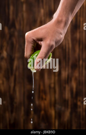 Hand squeeze lime with lime drop on dark wooden background Stock Photo