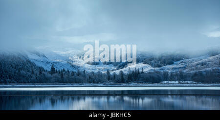 Winter scene at Loch Carron, Torridon, Scotland, with snow covered hills reflected in the loch on a cold winter morning, snow showers in the distance Stock Photo