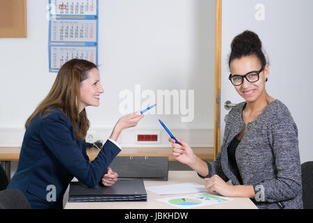 Zwei Frauen sind bei einer Besprechung und sitzen am Tisch im Büro. Beide Frauen haben einen Stift in der Hand. Stock Photo