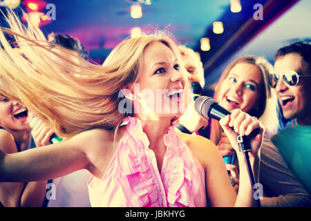 Portrait of joyous girl singing at party on background of happy friends Stock Photo