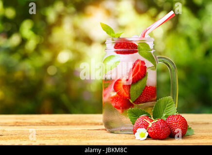 strawberry lemonade in mason jar on wooden table with blurred sunshine natural background. Summer refreshing drink. Cold detox water. Strawberry cockt Stock Photo
