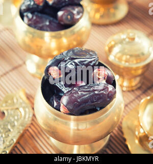 Dried date palm fruits or kurma, ramadan food which eaten in fasting month. Pile of fresh dried date fruits in golden metal bowl. Stock Photo