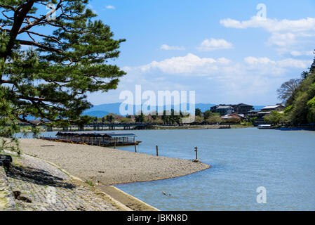 Katsura river at Arashiyama, sightseeing boats  moored at the riverbank and Togetsukyo bridge in the background. Stock Photo