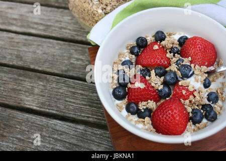 Healthy breakfast bowl. Granola in white bowl with greek yogurt and berries on wooden background Stock Photo