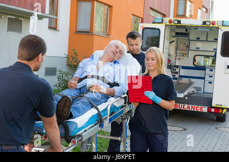 Emergency team assisting injured elderly man lying on stretcher outdoors Stock Photo