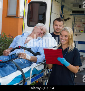 Emergency team treating injured elderly patient lying on stretcher outdoors Stock Photo